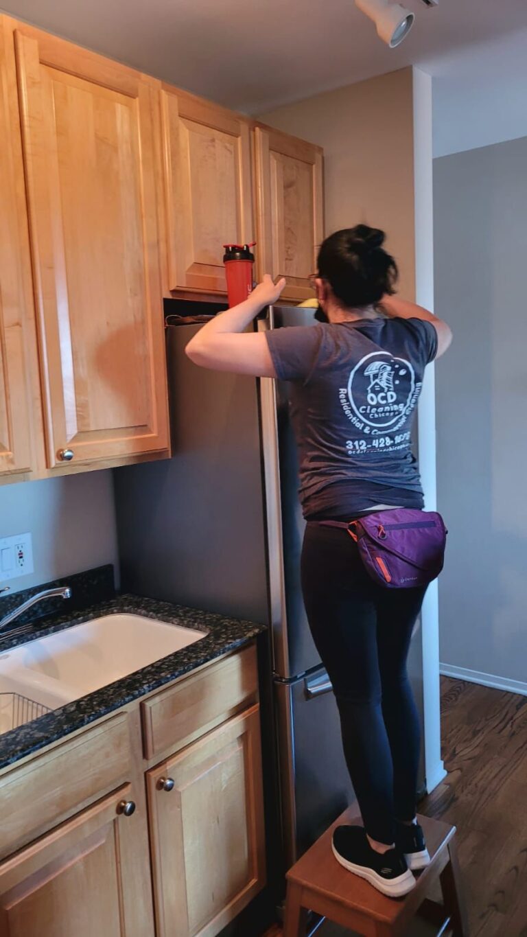 OCD professional cleaning the top of a refrigerator